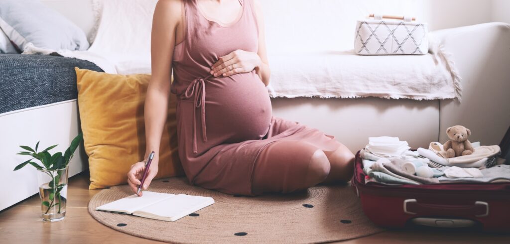 Expectant mother with suitcase of baby stuff preparing for newborn birth during pregnancy.