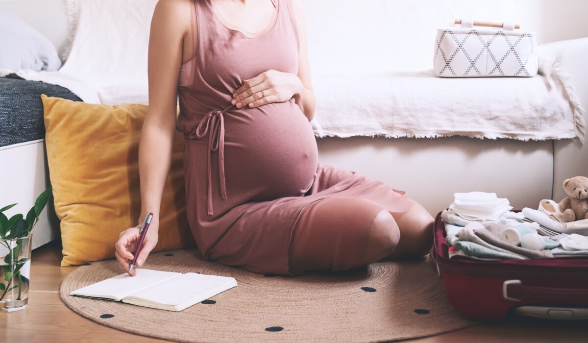 Expectant mother with suitcase of baby stuff preparing for newborn birth during pregnancy.